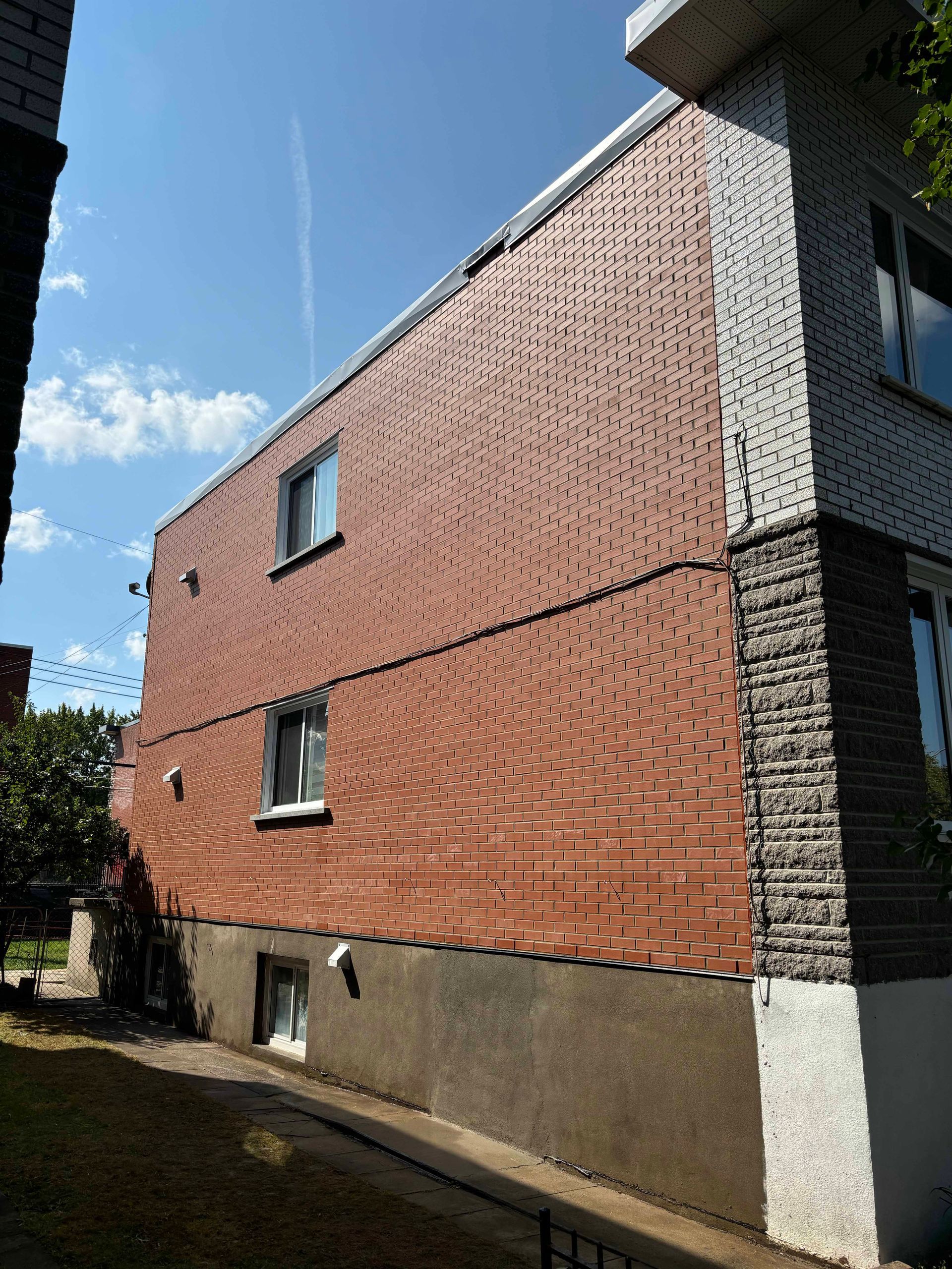 Façade en briques d'un bâtiment avec trois fenêtres par une journée ensoleillée.