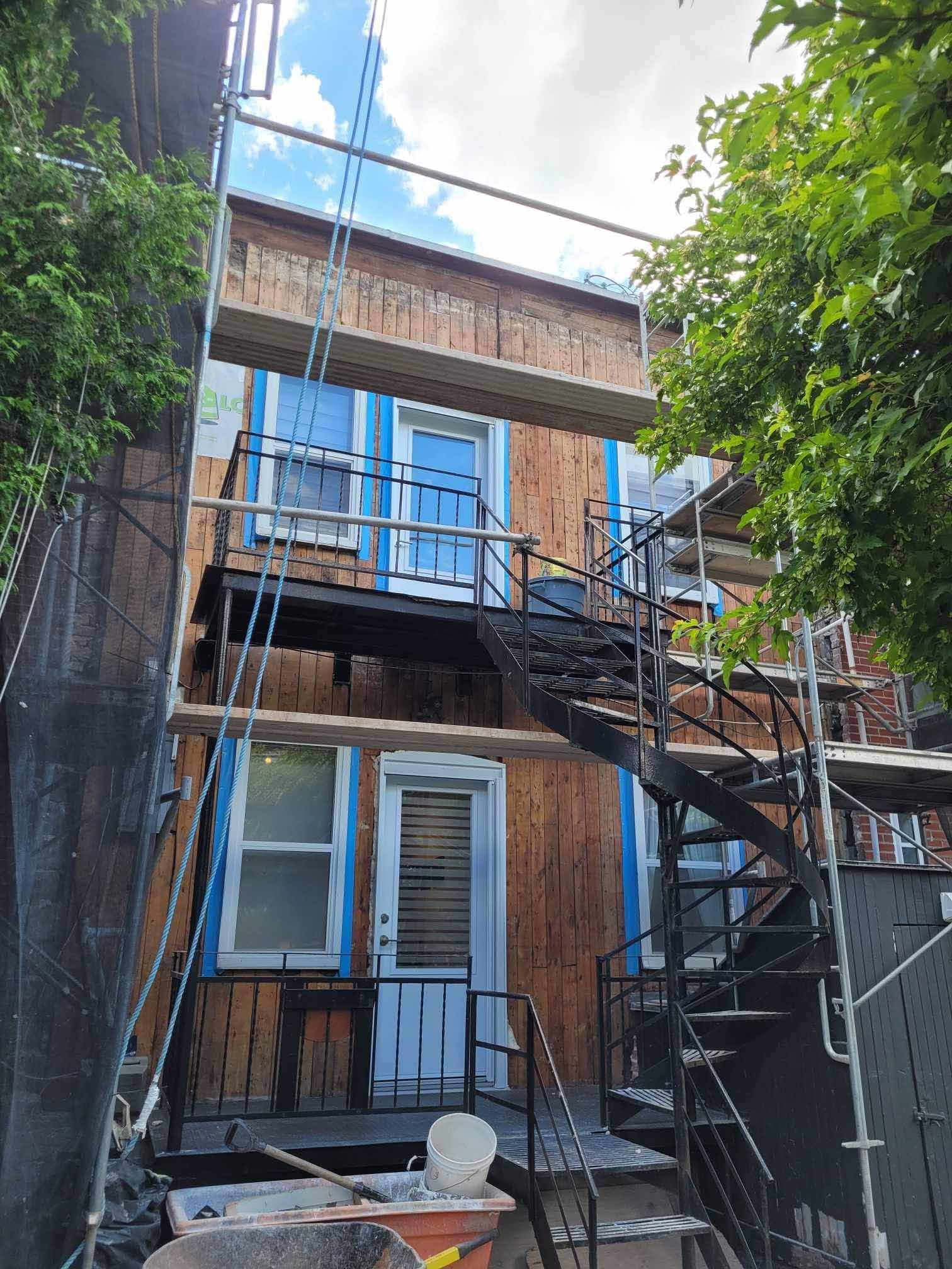 Extérieur d'un bâtiment en construction avec un escalier de secours métallique et des échafaudages.