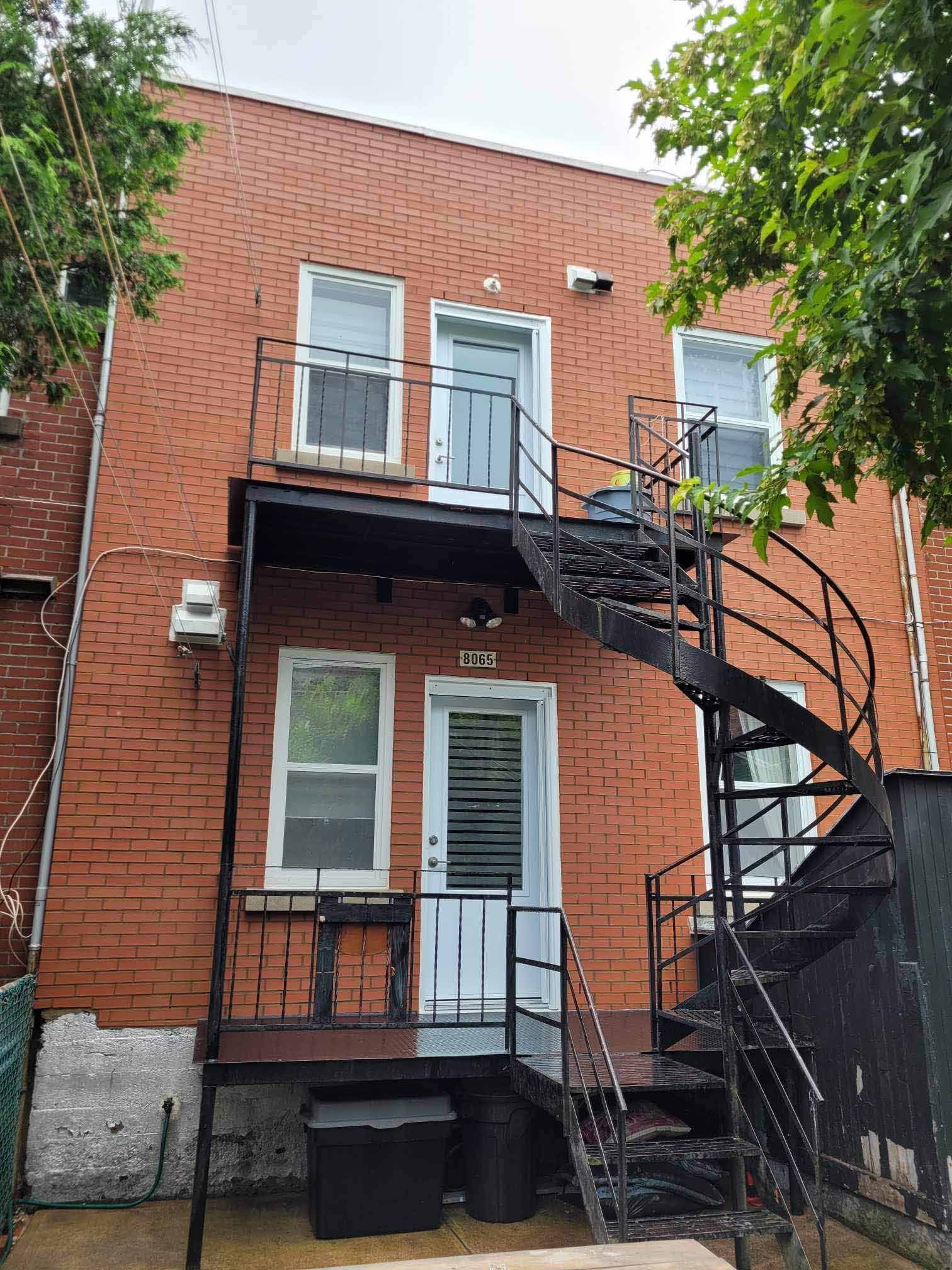 Bâtiment en briques avec escaliers de secours et portes noires.