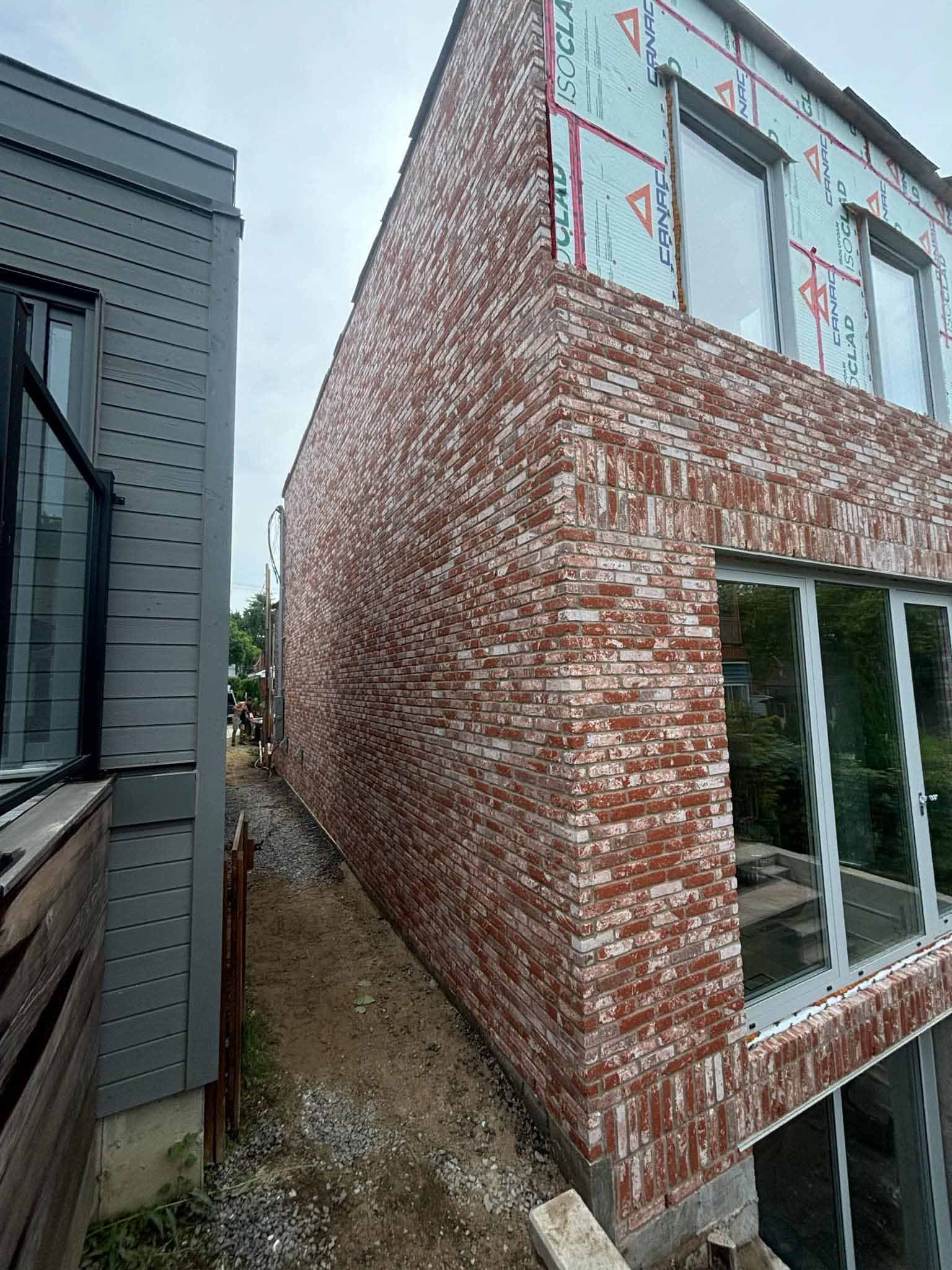 Façade en briques d'un bâtiment jouxtant une structure revêtue d'un bardage gris, avec une allée étroite.