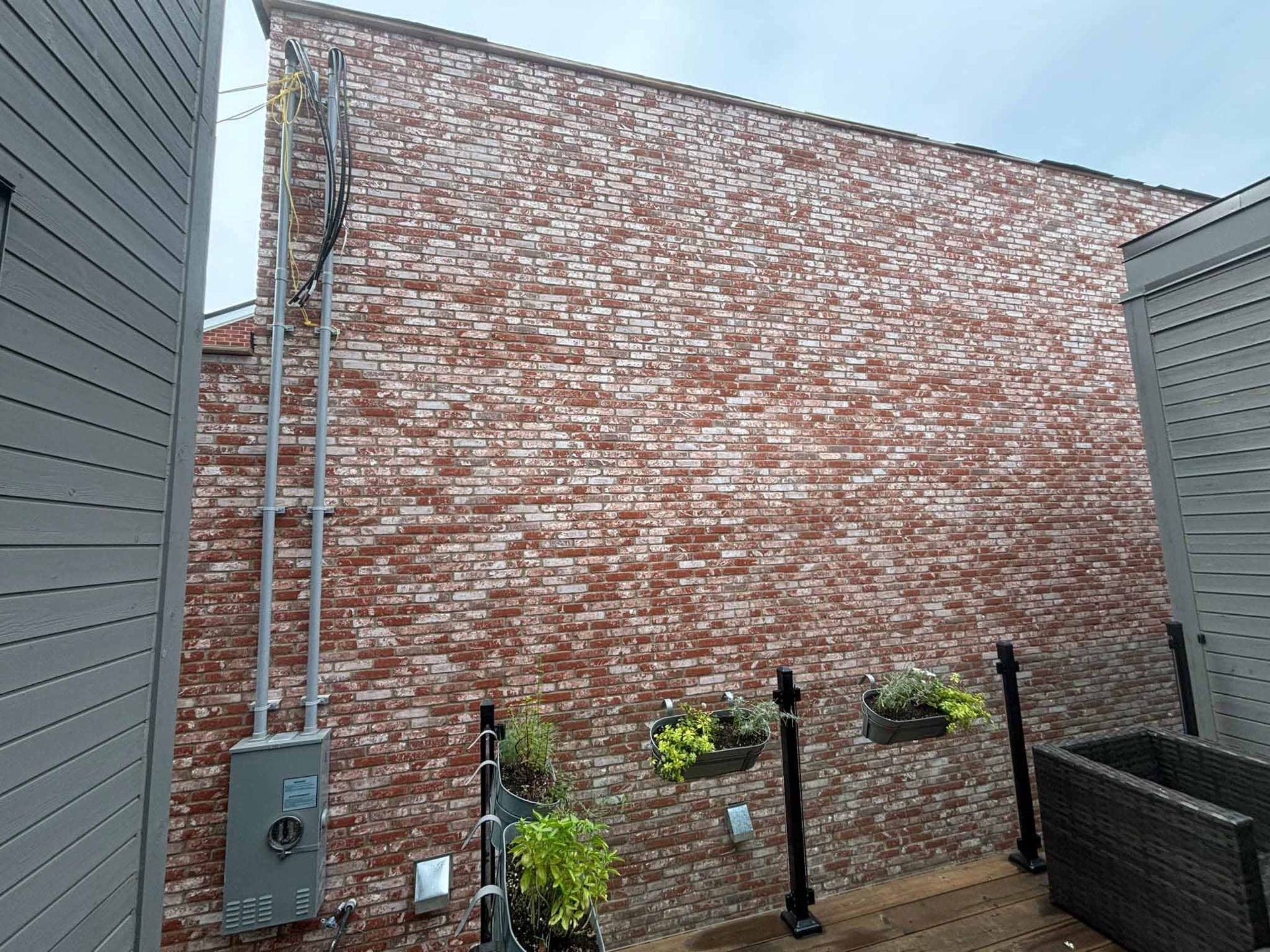 Mur en briques avec conduits électriques et petit patio avec jardinières.