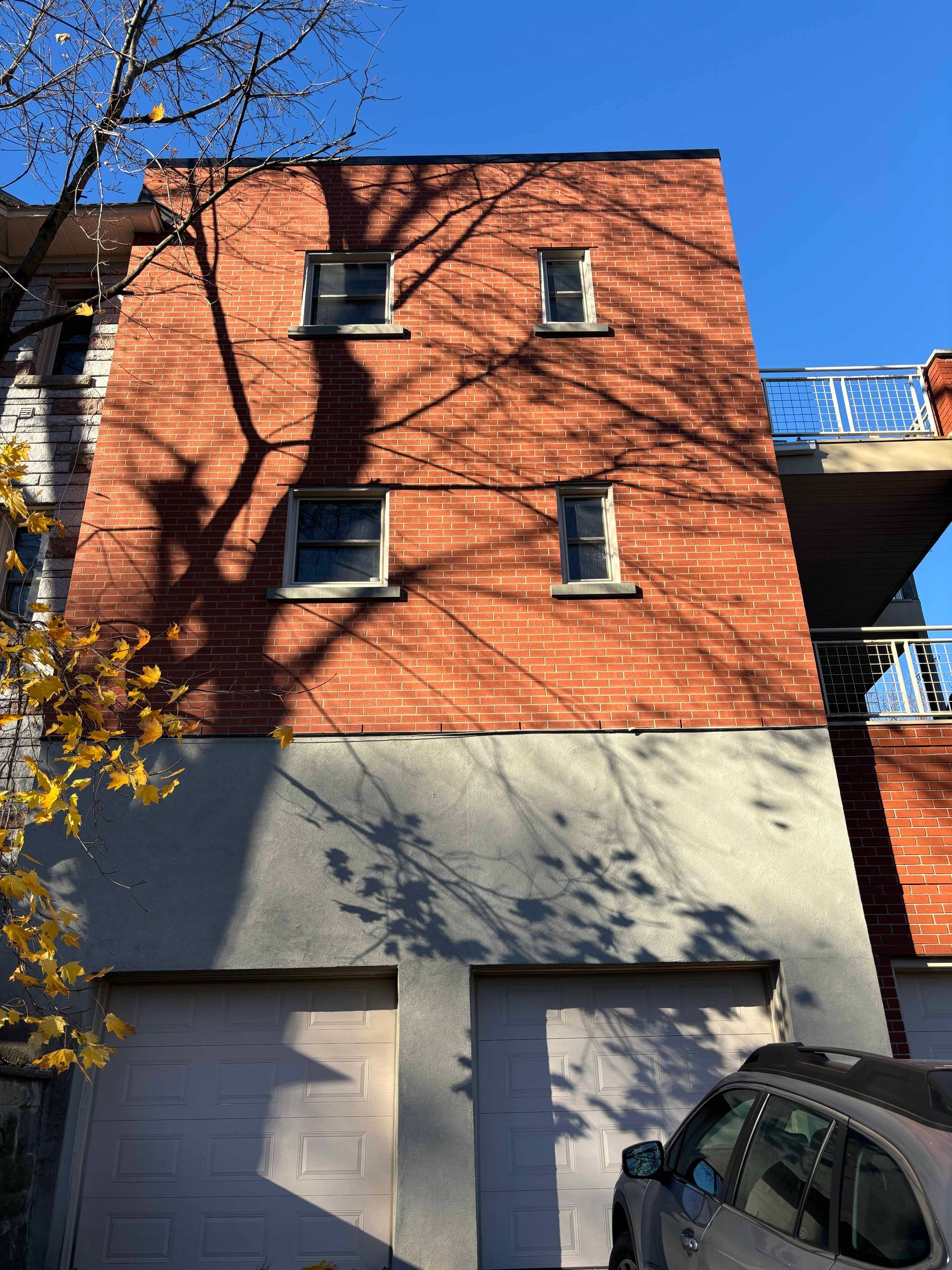 Bâtiment en briques avec portes de garage, fenêtres et ombres d'arbres.