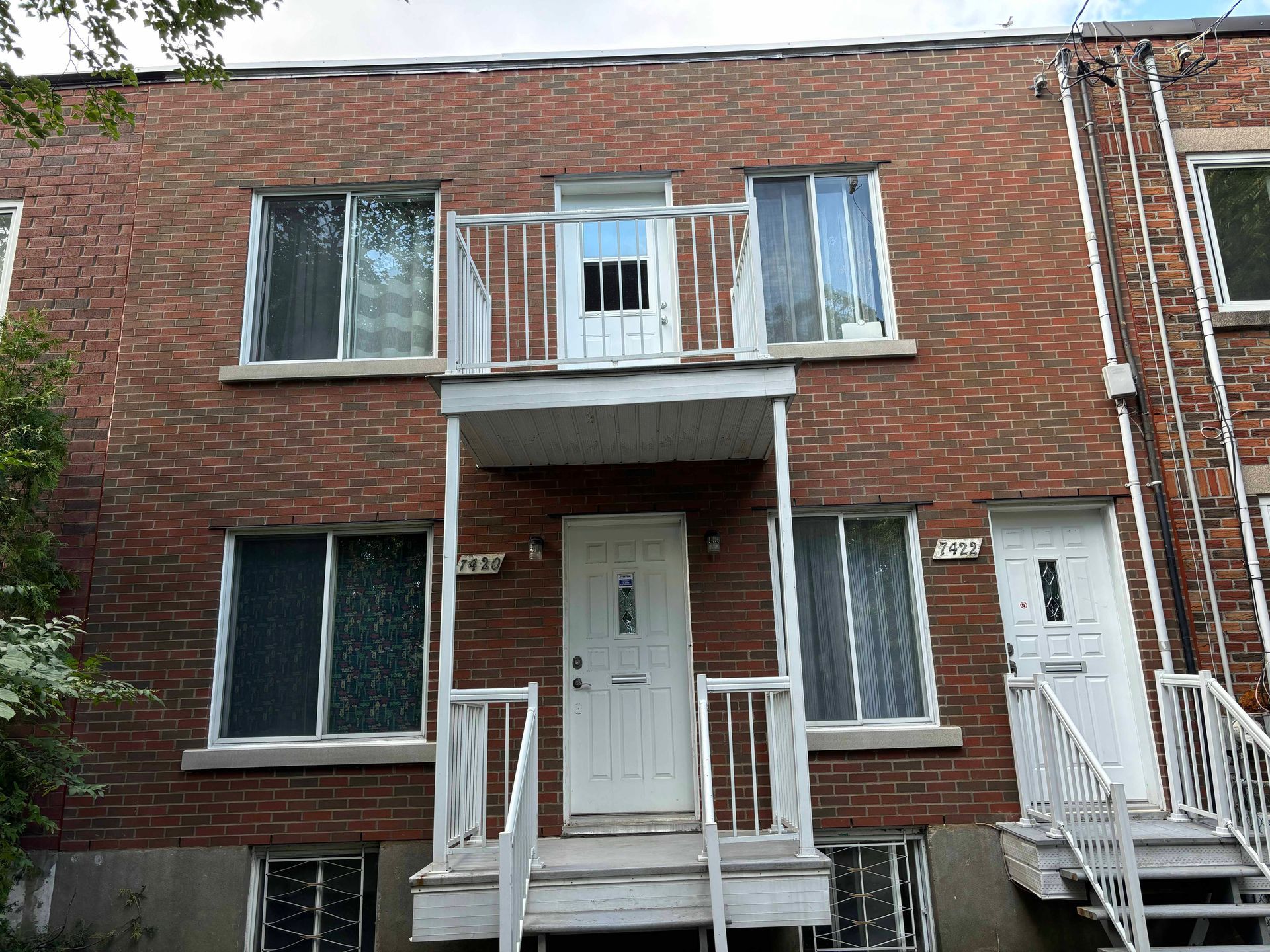 Bâtiment en briques avec portes, fenêtres et balcons blancs.