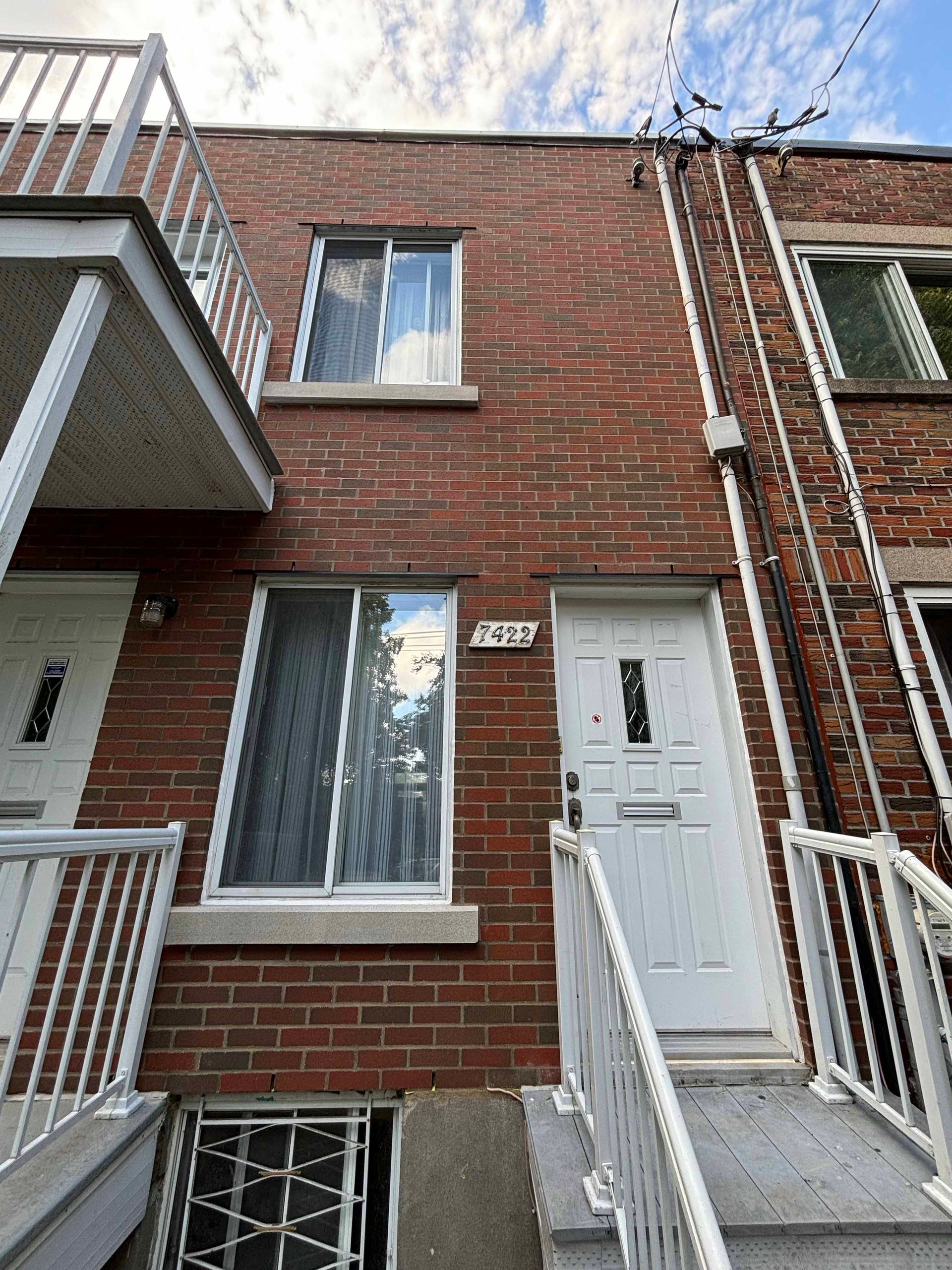 Maison de ville en briques avec porte et fenêtre blanches, escalier et balcon par une journée ensoleillée.