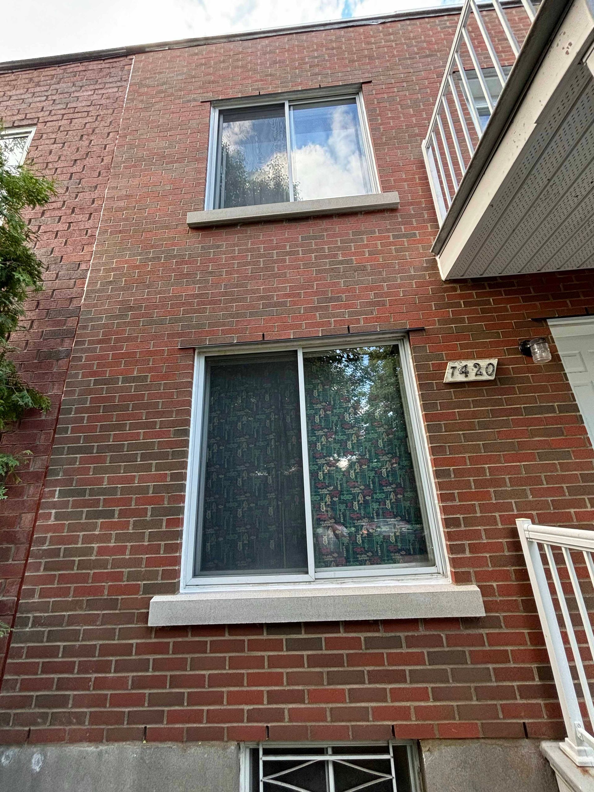 Façade en briques d'un immeuble avec deux fenêtres et un petit balcon.