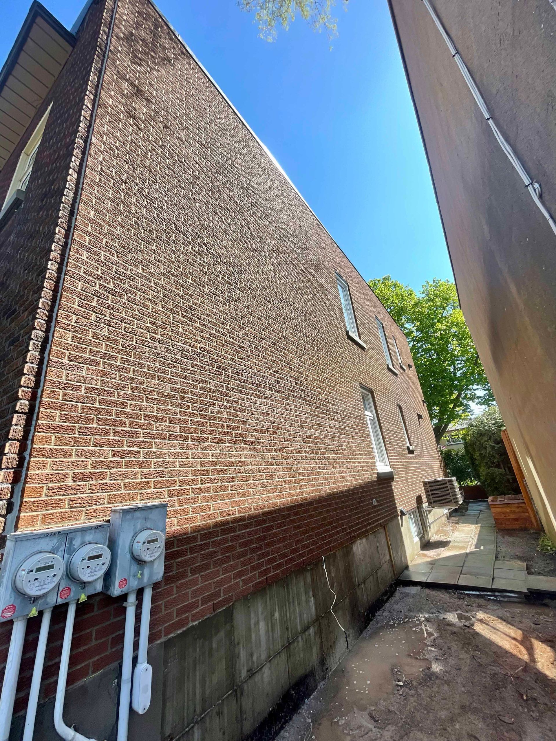Extérieur d'un bâtiment en briques avec compteurs électriques, allée et ciel bleu.