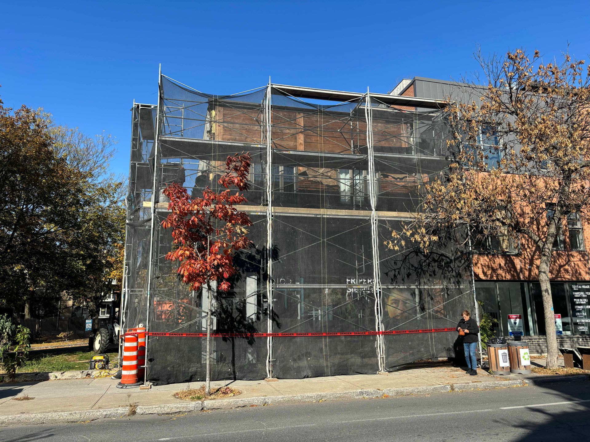 Façade d'immeuble recouverte d'un filet noir, ruban adhésif rouge, trottoir. Feuilles d'automne.