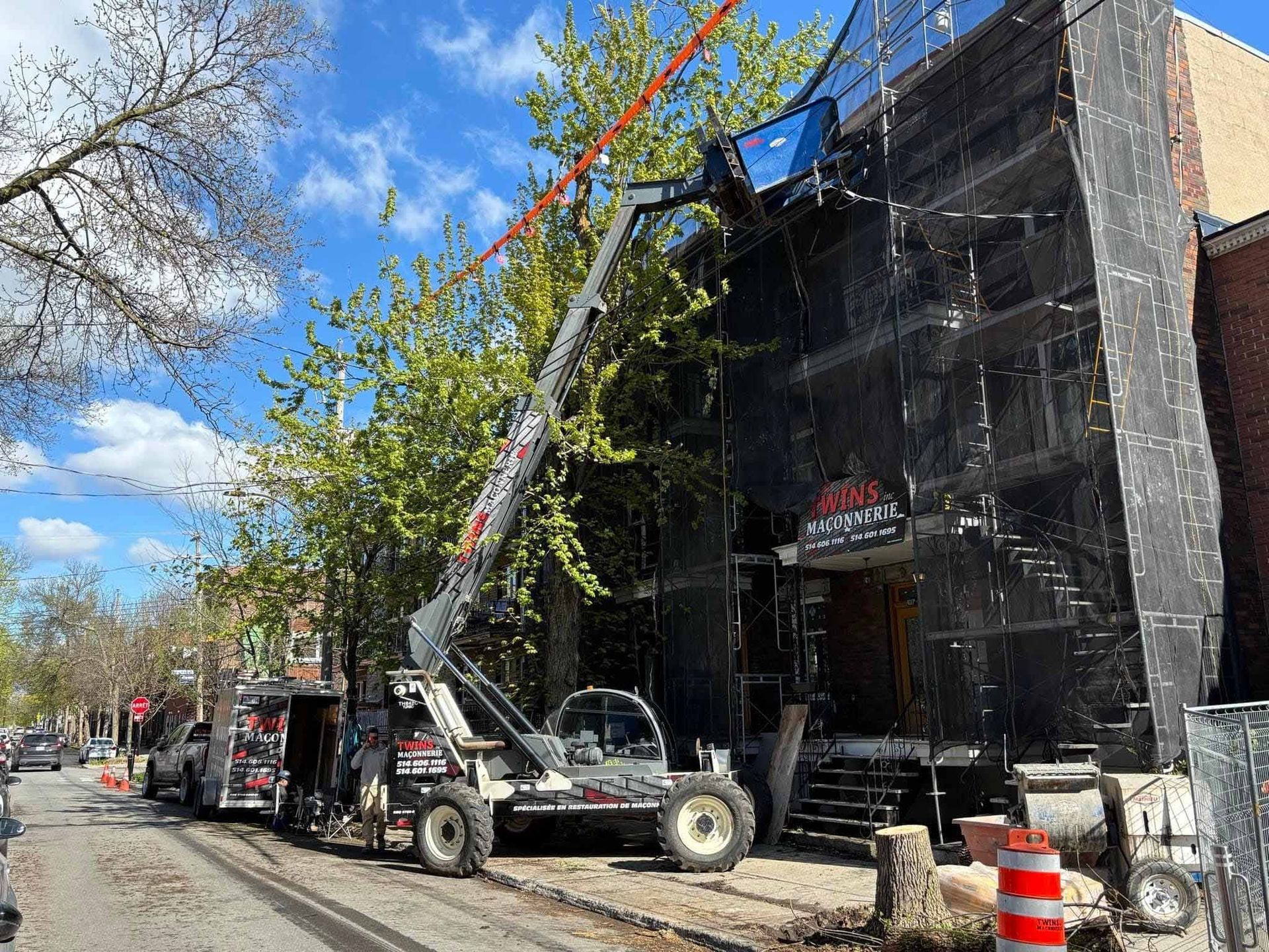 Un chantier de construction avec une grande grue à l'œuvre sur un bâtiment. Un grillage noir recouvre la façade.