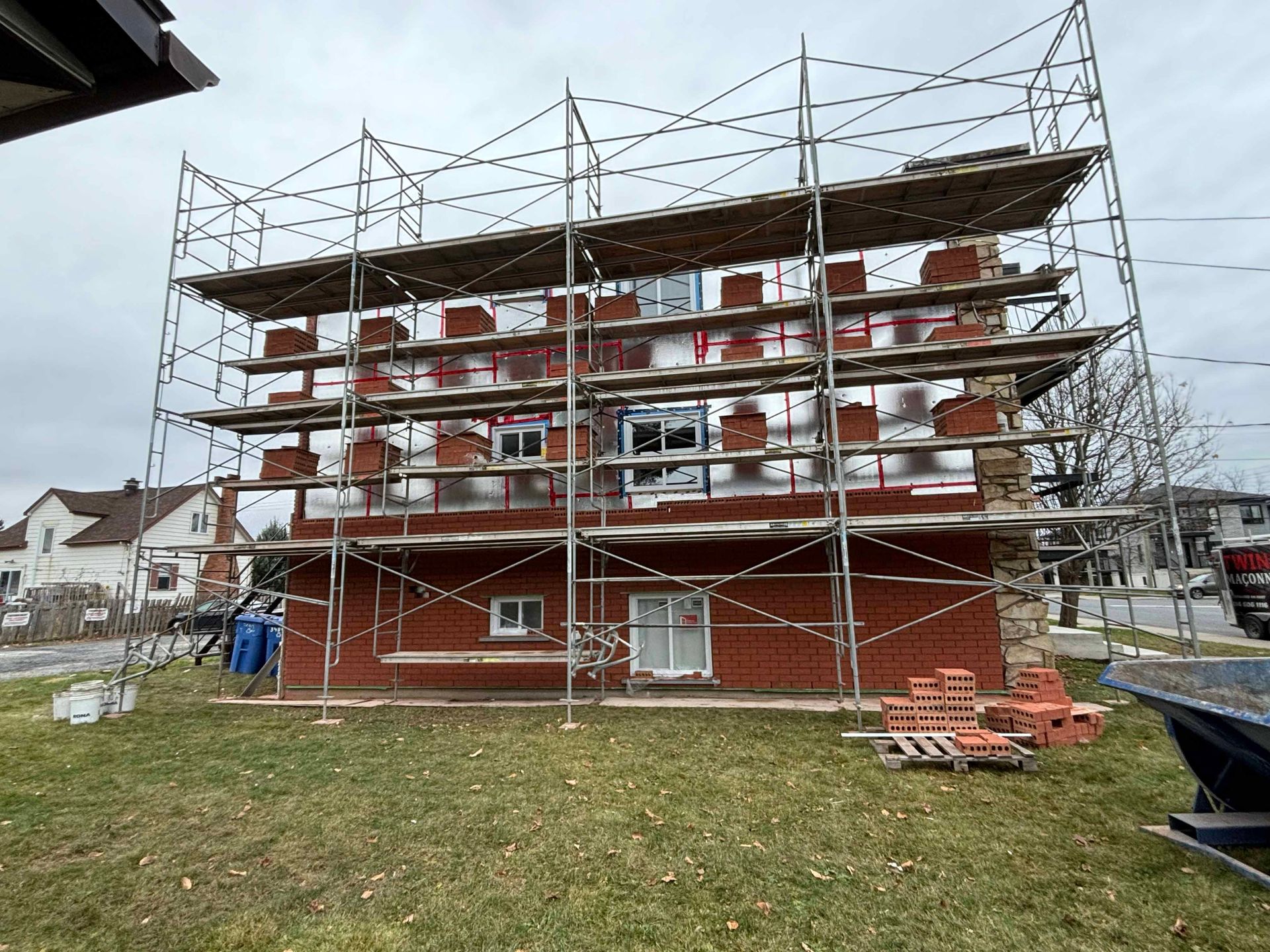 Bâtiment en construction avec échafaudages et briques. Vue extérieure d'un bâtiment en briques rouges avec isolation argentée.