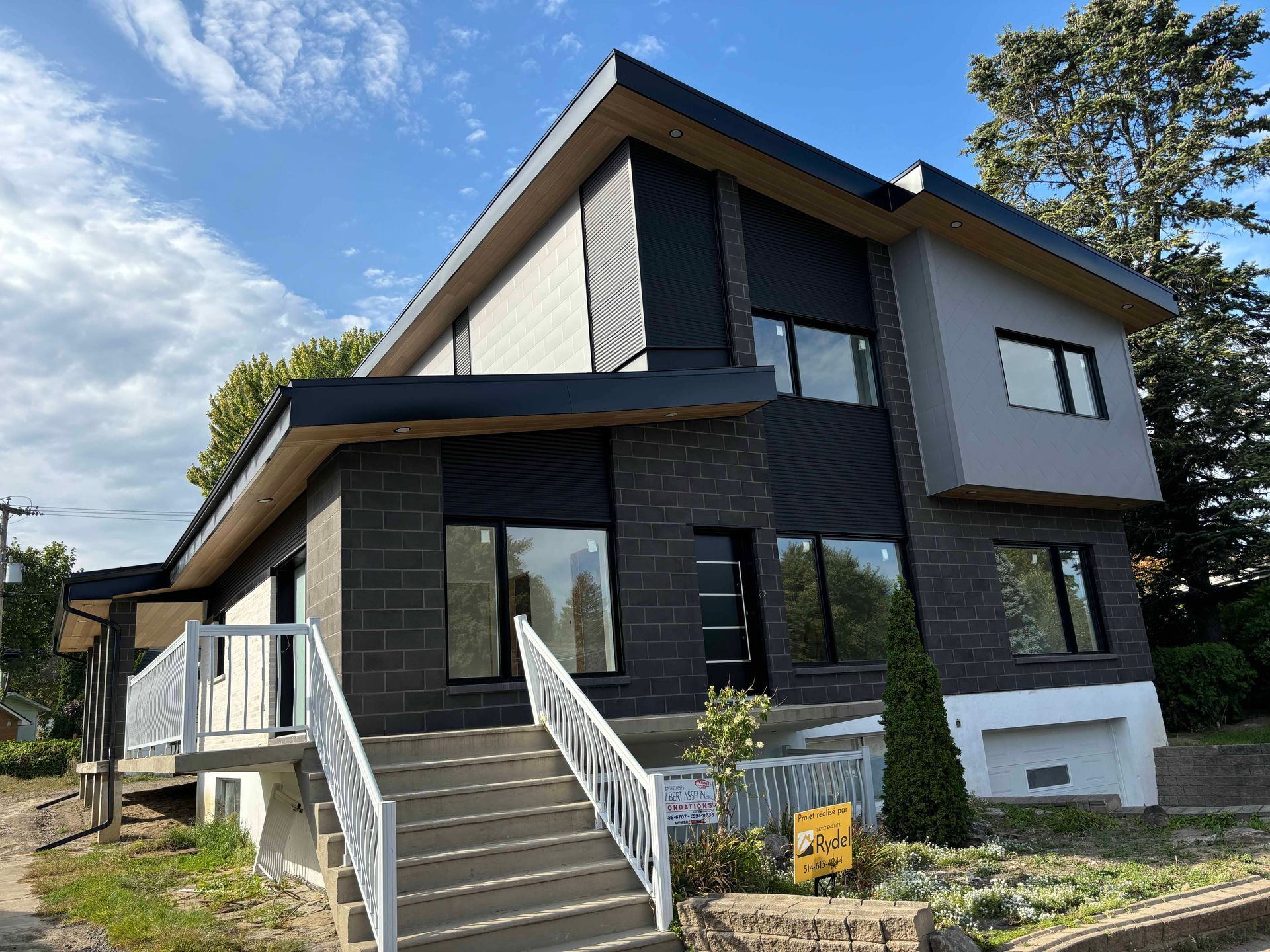 Maison moderne à deux étages avec briques et bardage gris foncé, touches de gris clair, grandes fenêtres et escalier d'entrée.
