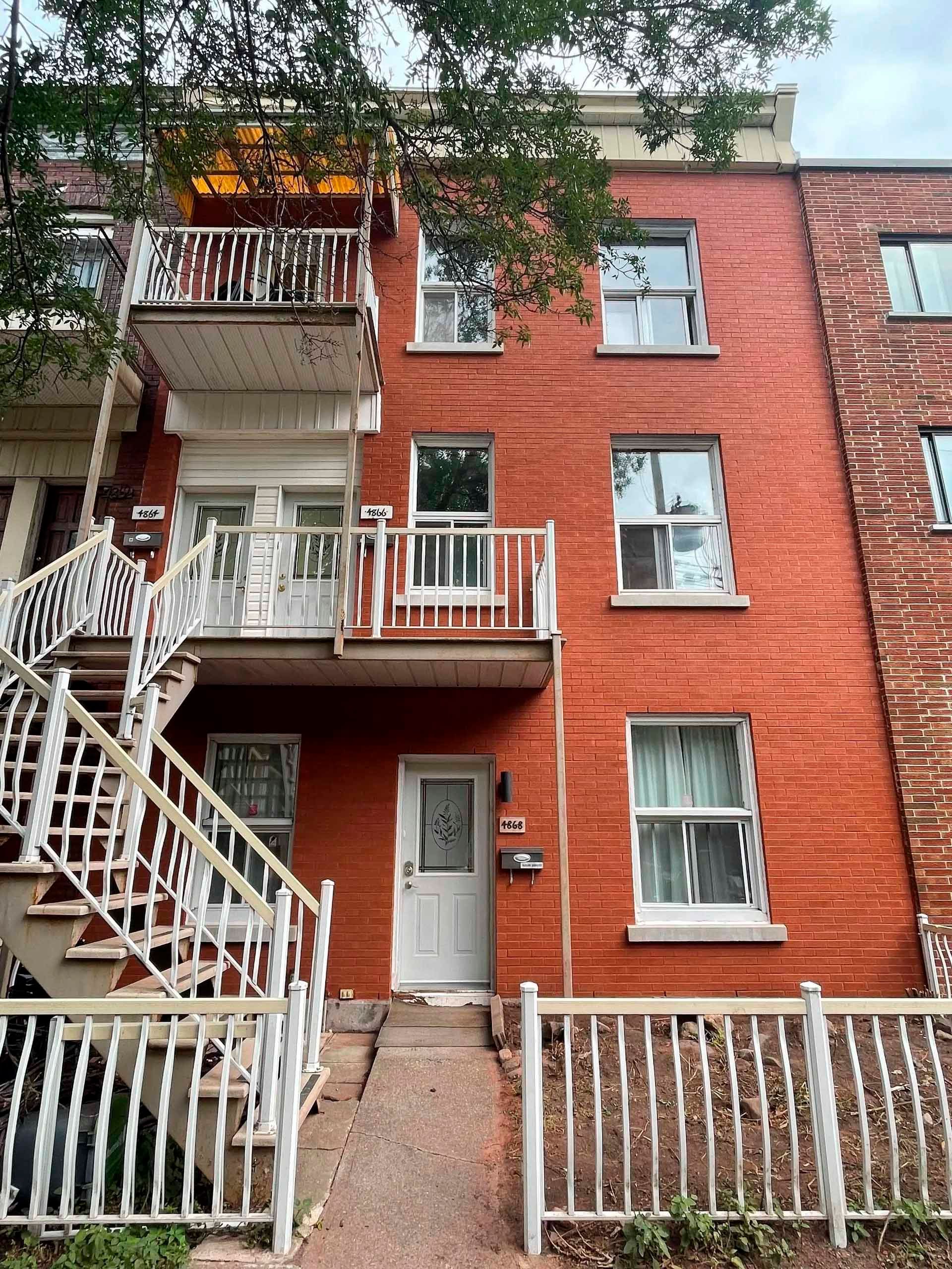 Bâtiment en briques rouges avec balcons et escaliers blancs, porte d'entrée au rez-de-chaussée.