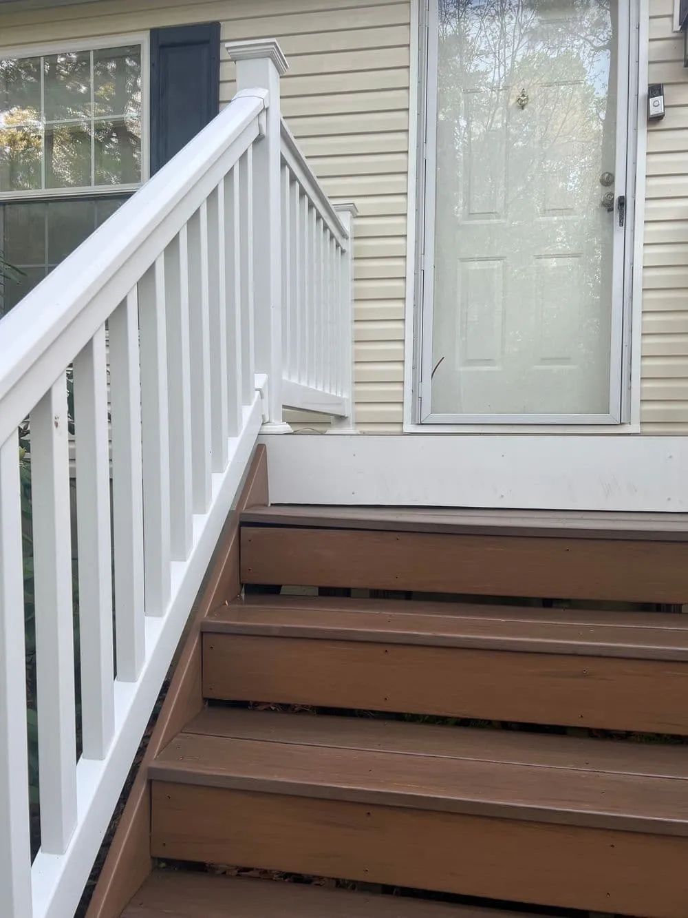 Wooden steps leading up to a white-railed porch and front door. Brown steps, white railing, beige siding.