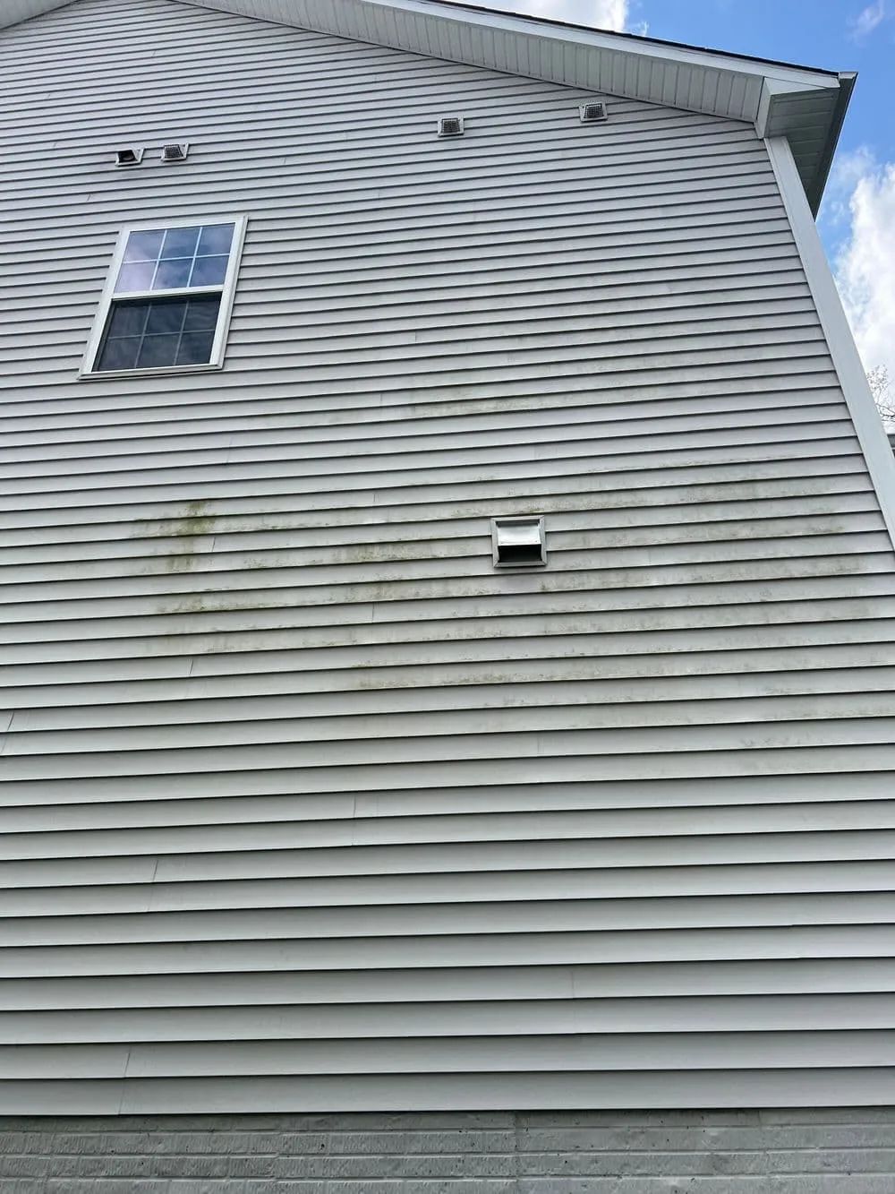 Gray vinyl siding with a single window and exhaust vent on a house exterior.