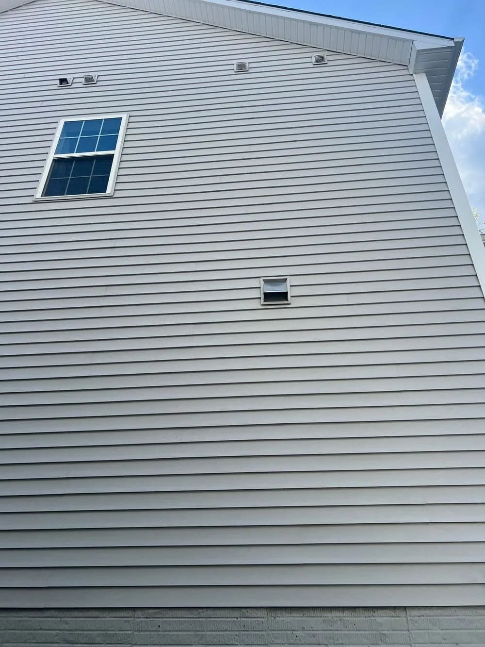 Gray house siding with a window and a vent. Blue sky is visible.