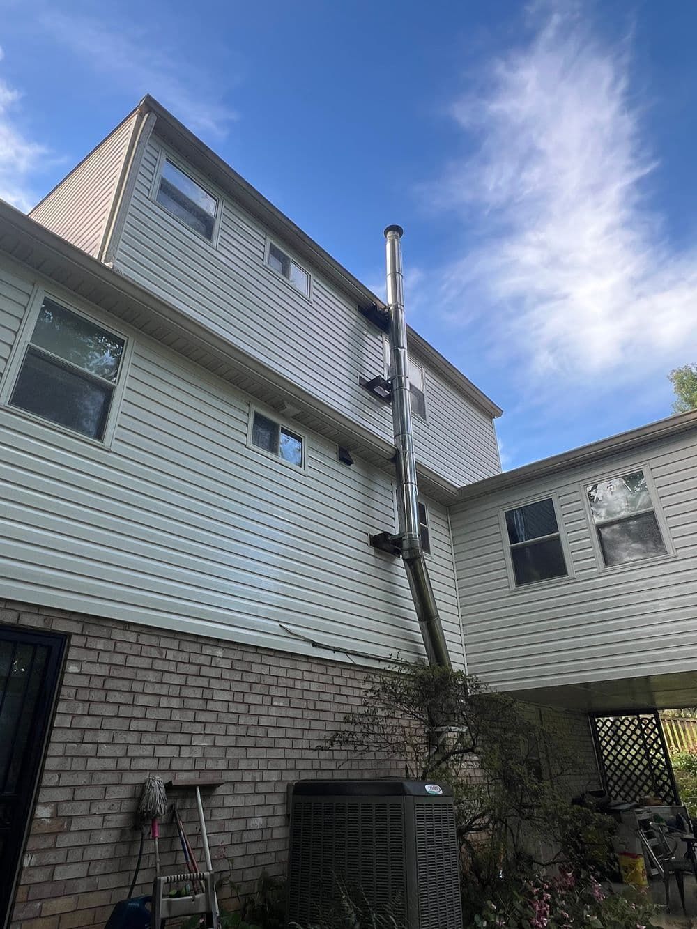 Exterior of a two-story house with a metal chimney running up the siding, against a blue sky.