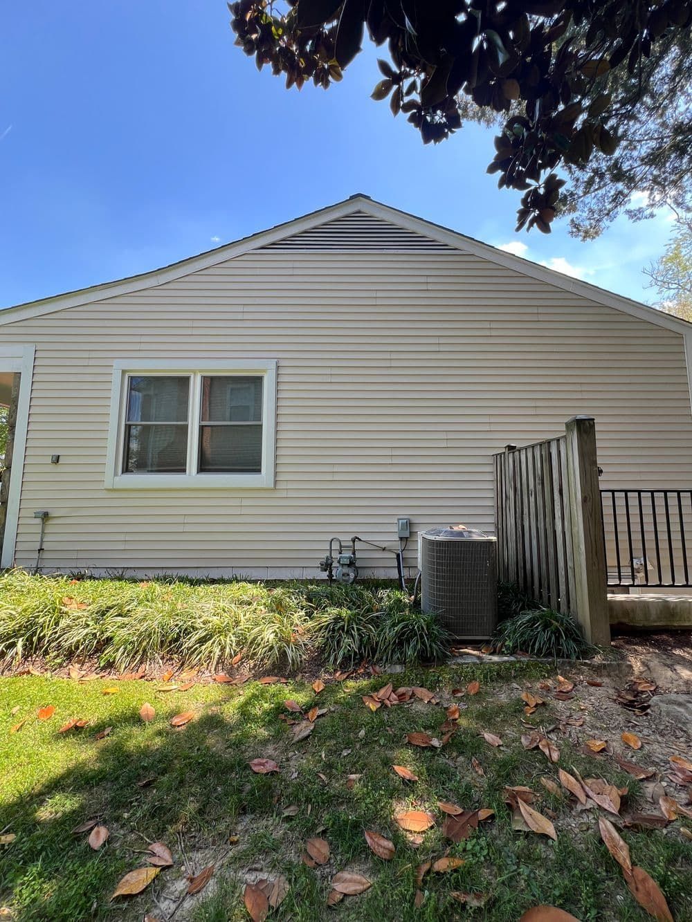Beige house with a window, air conditioning unit, and wooden fence.