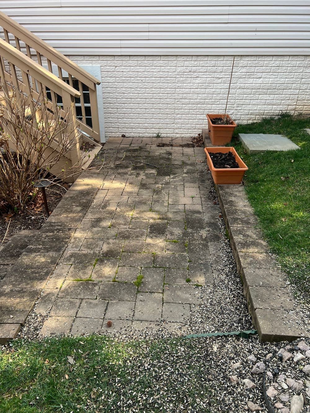 Brick patio with stairs, planters, and gravel path beside a building.
