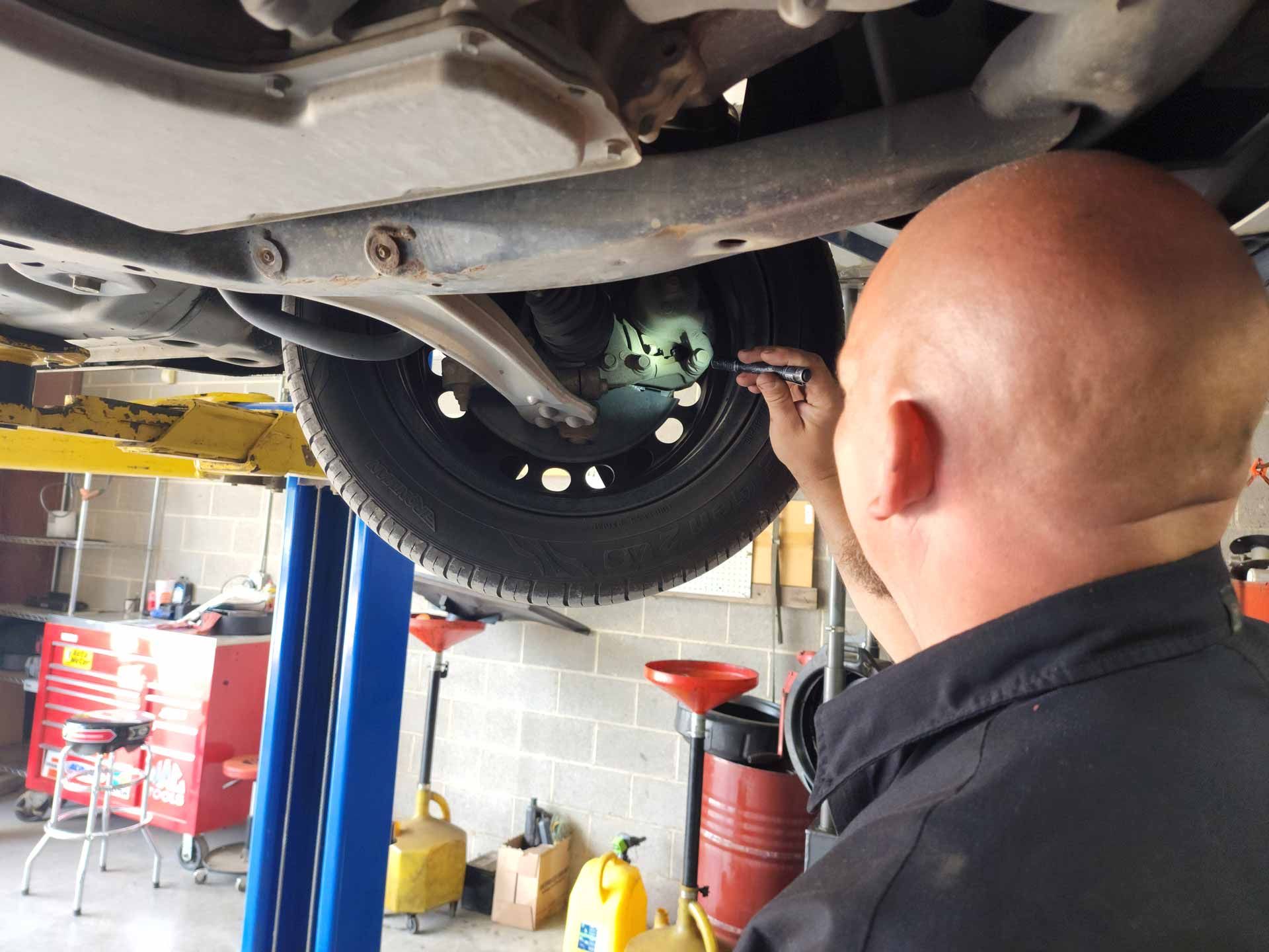 A bald man is working under a car in a garage