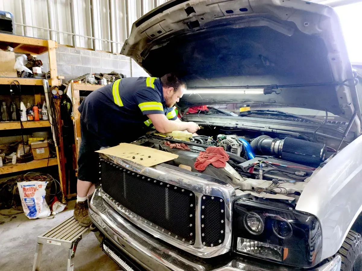 A man is working under the hood of a truck in a garage.