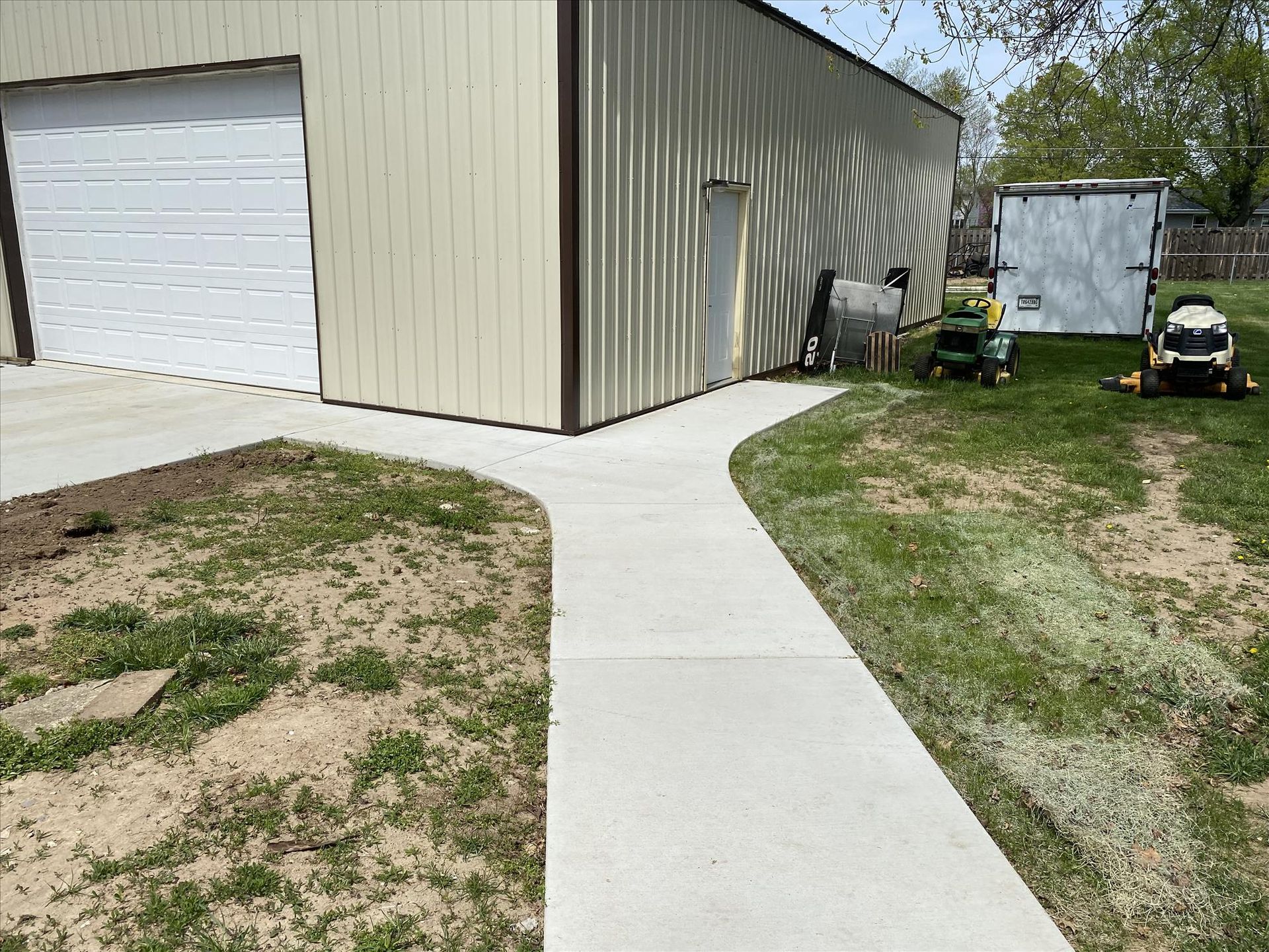 A concrete walkway leading to a garage and a lawn mower.
