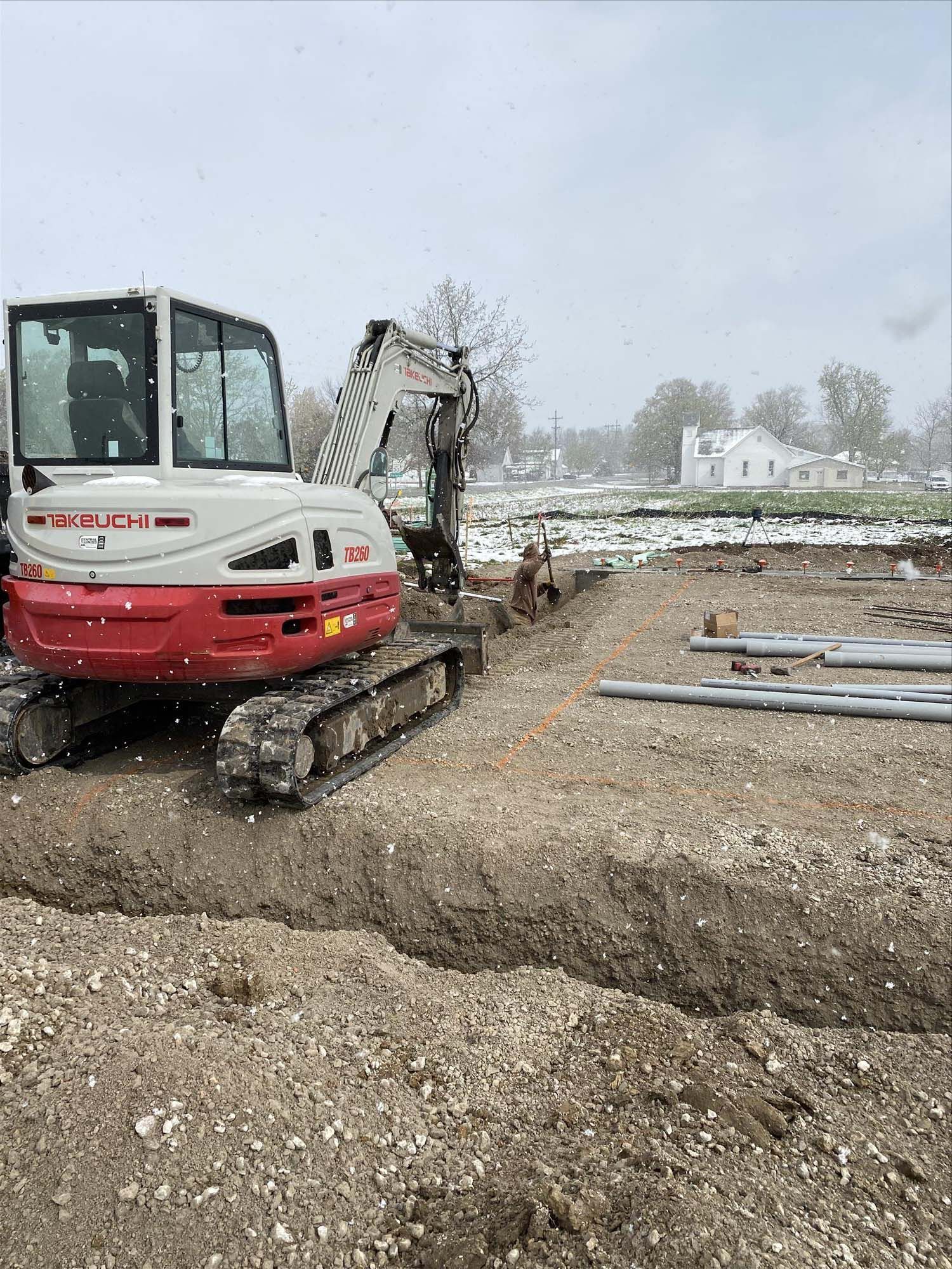 A red and white excavator is digging a hole in a dirt field.