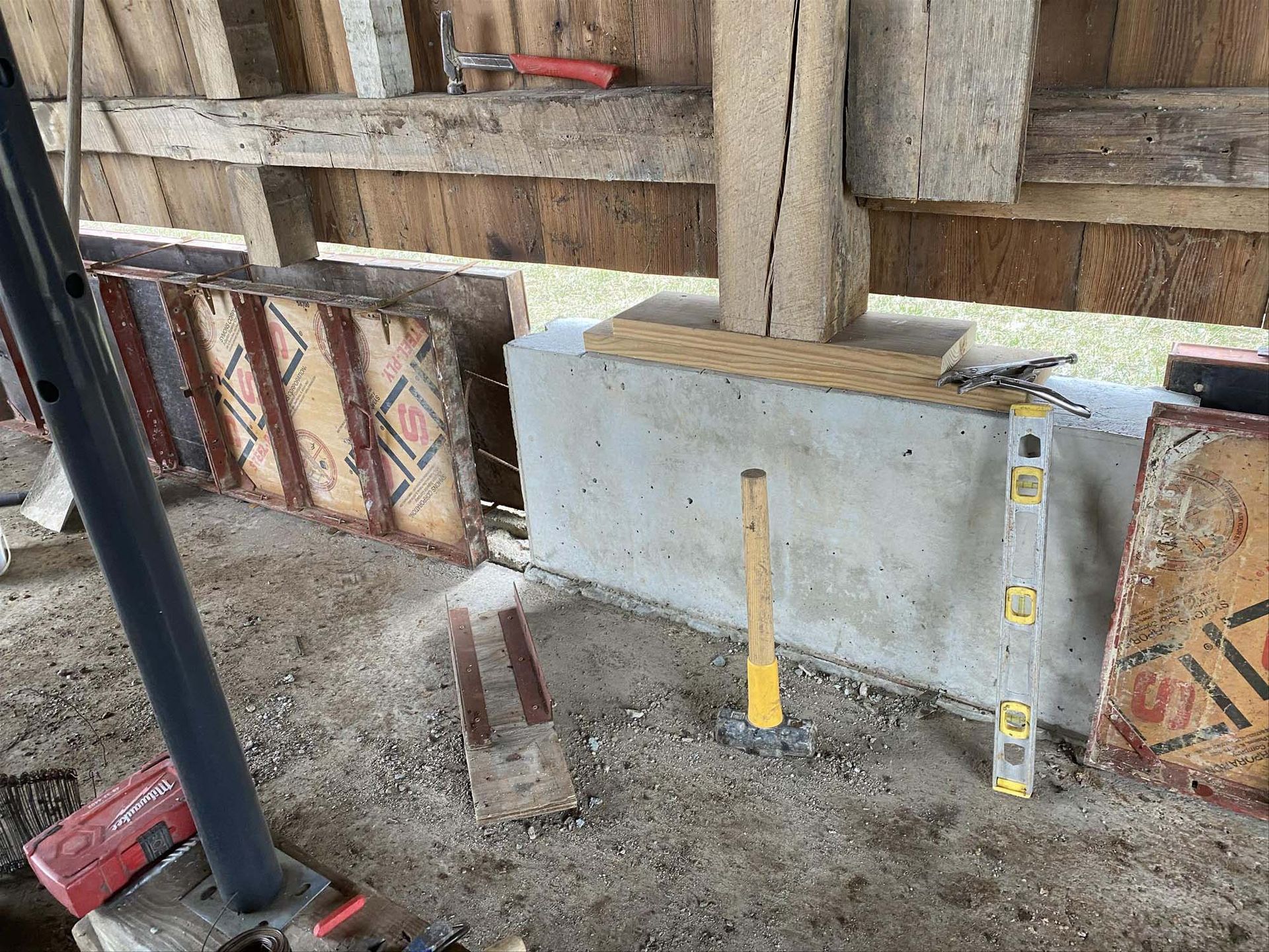 A hammer and a level are sitting on the ground in front of a wooden wall.