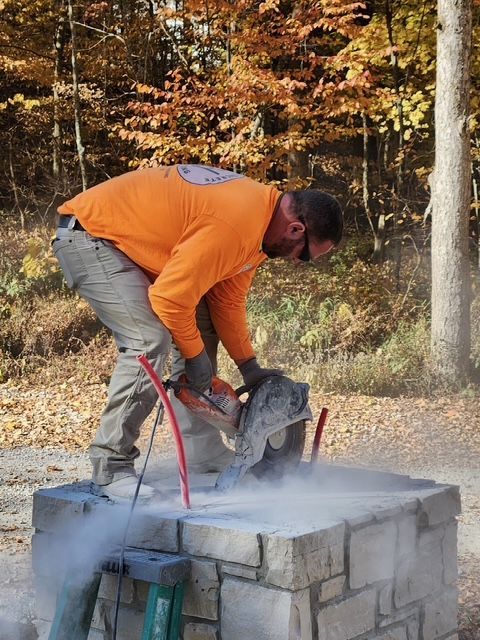 A man in an orange shirt is cutting a stone wall with a saw.
