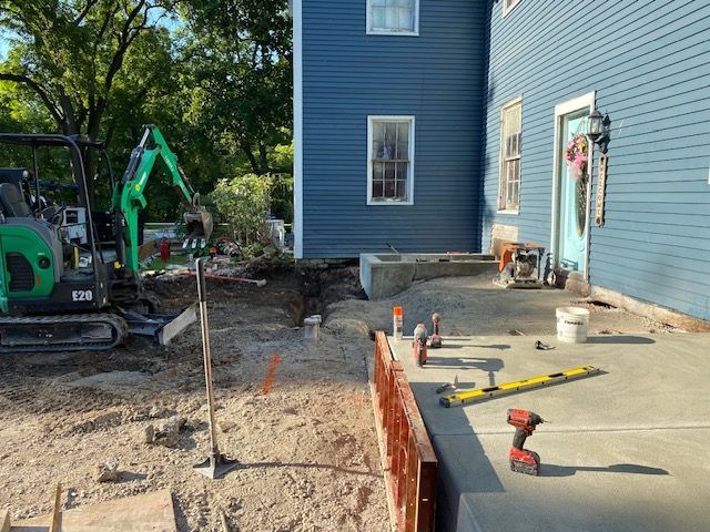 A blue house is being remodeled and a concrete patio is being built in front of it.