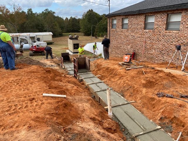 A group of construction workers are working on a sidewalk in front of a brick house.