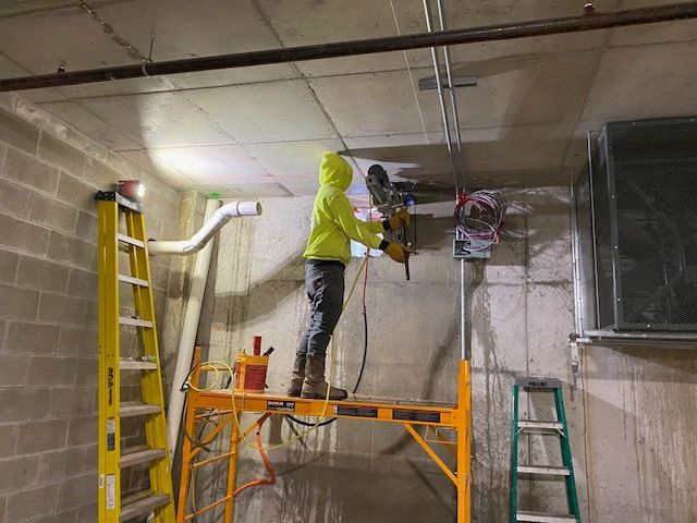 A man is standing on a scaffolding in a room using a drill.