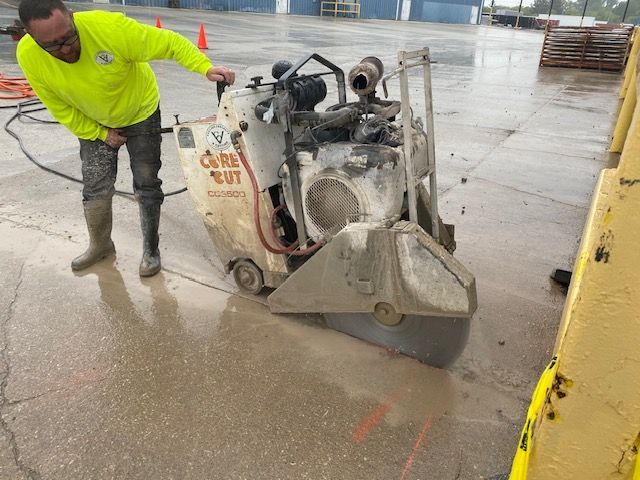 A man is using a concrete saw to cut a hole in the ground.