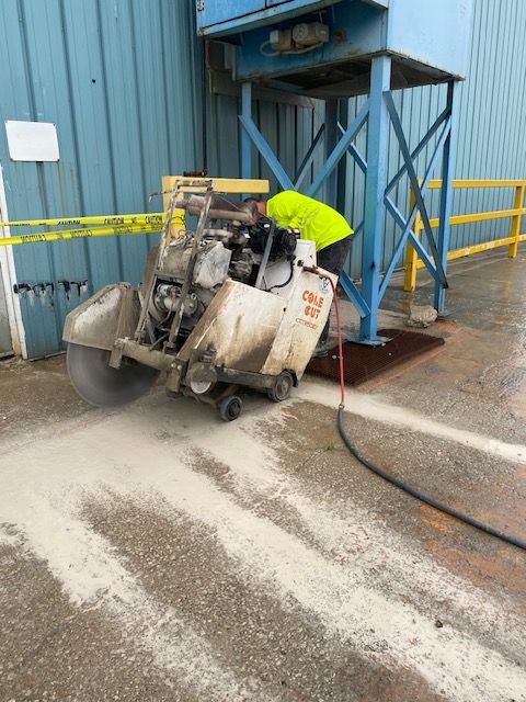 A man is using a machine to cut concrete in front of a building.