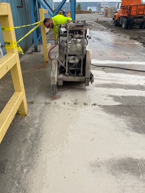 A man is using a machine to cut concrete in a parking lot