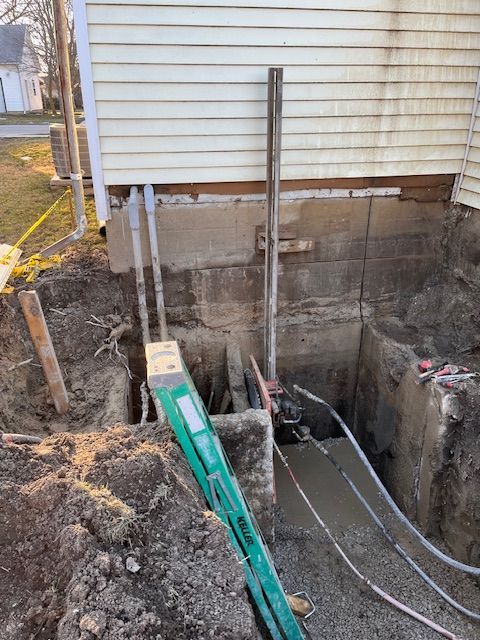A green ladder is sitting next to a hole in the ground in front of a house.