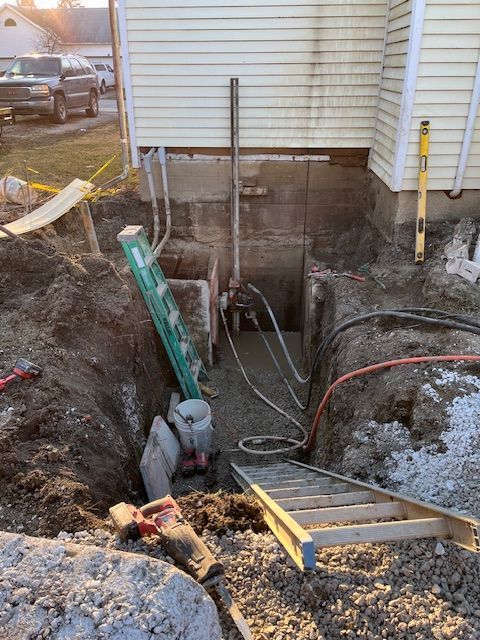 A hole in the ground next to a house with a ladder in it.