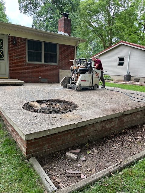 A man is using a machine to cut a concrete patio in front of a house.