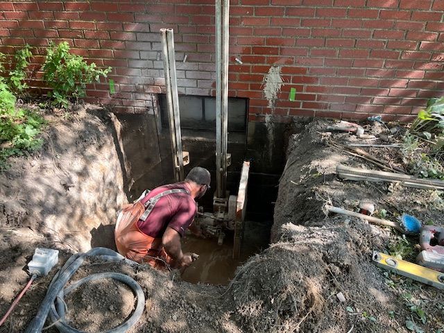 A man is digging a hole in the ground in front of a brick building.