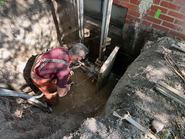 A man is digging a hole in the ground in front of a brick wall.