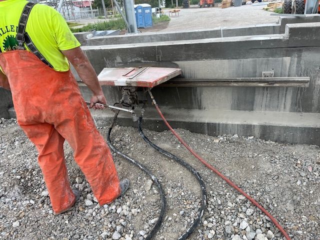 A man in orange overalls is cutting a concrete wall with a saw.