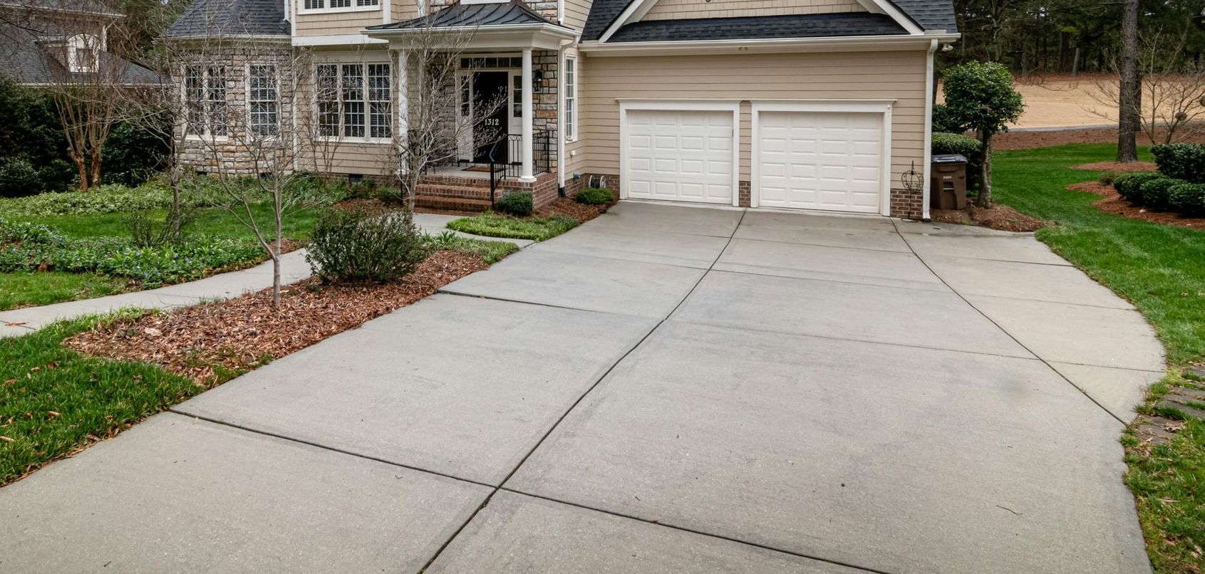 A concrete driveway leading to a house with two garage doors.