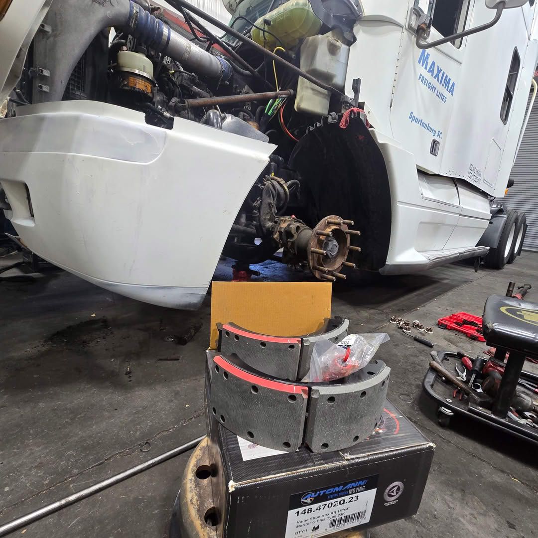 A truck is being repaired in a garage with a box of brake pads on the ground.