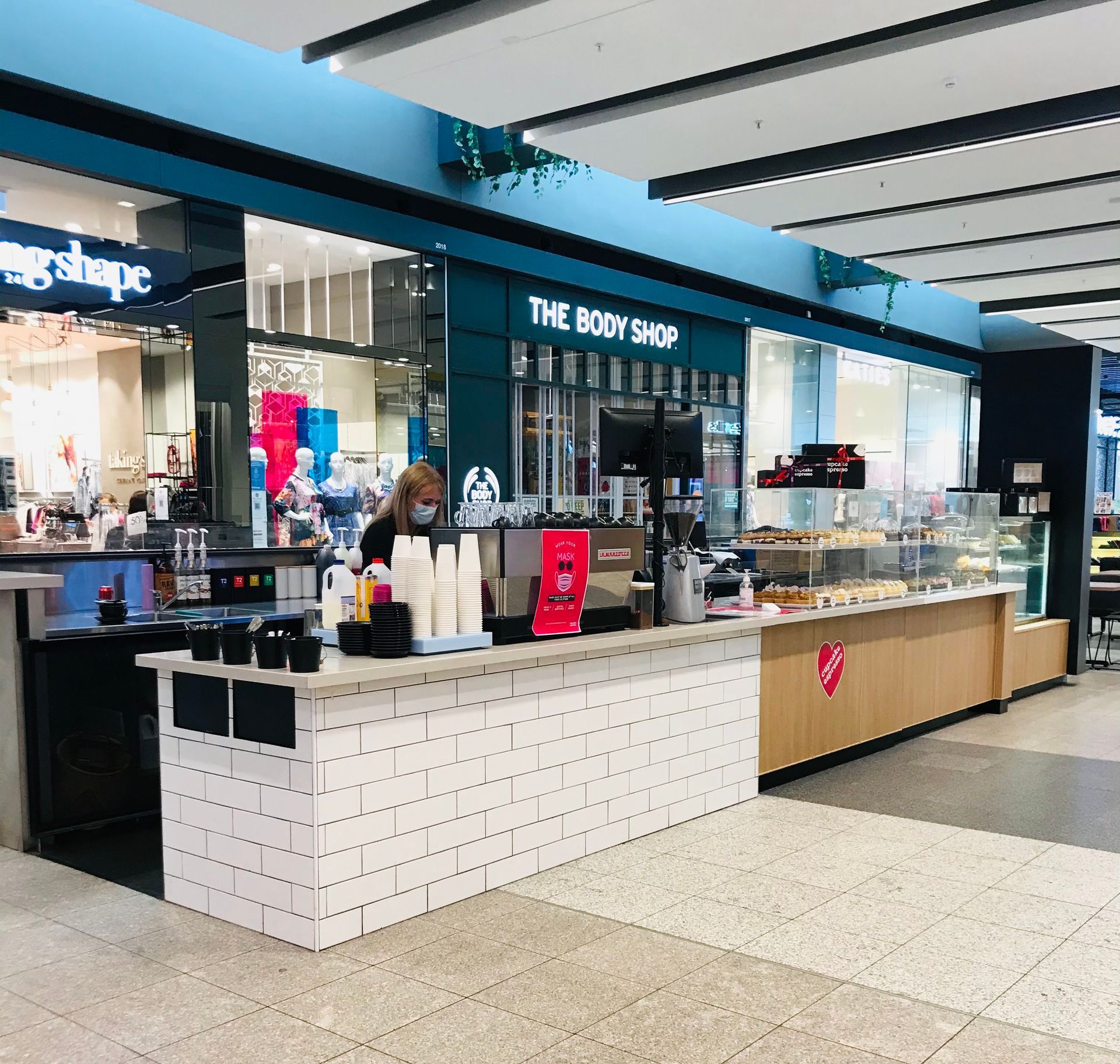 A Woman Is Standing Behind A Counter Of A Store Called The Body Shop — Nyon Shopfitters in Morisset, NSW