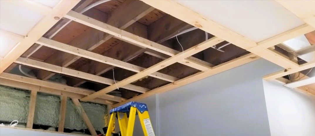 Exposed wooden beams in a building's basement ceiling with partial drywall installation