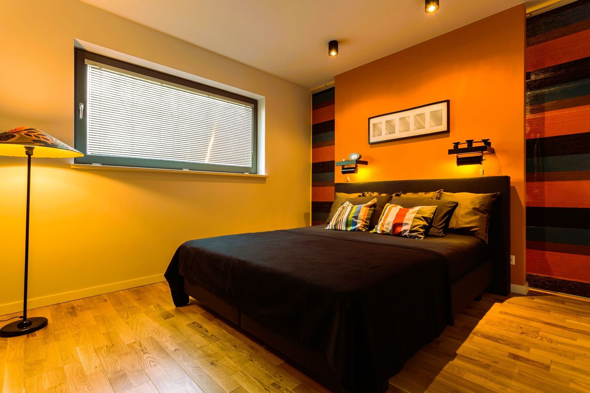 Cozy bedroom with black bedspread, striped pillows, stylish lamp, and orange accent wall