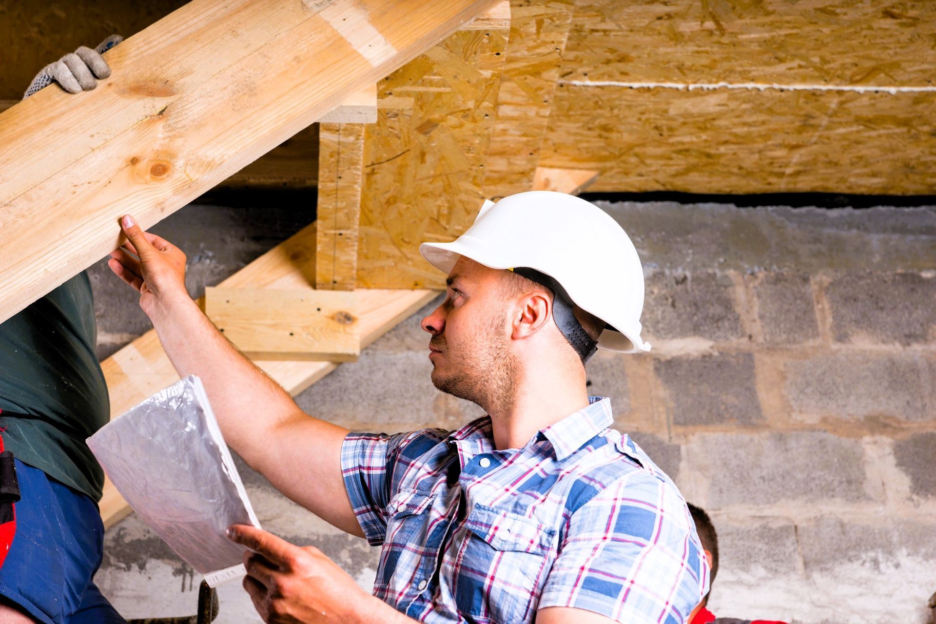 Basement finishing contractor in a hard hat inspecting wooden beams