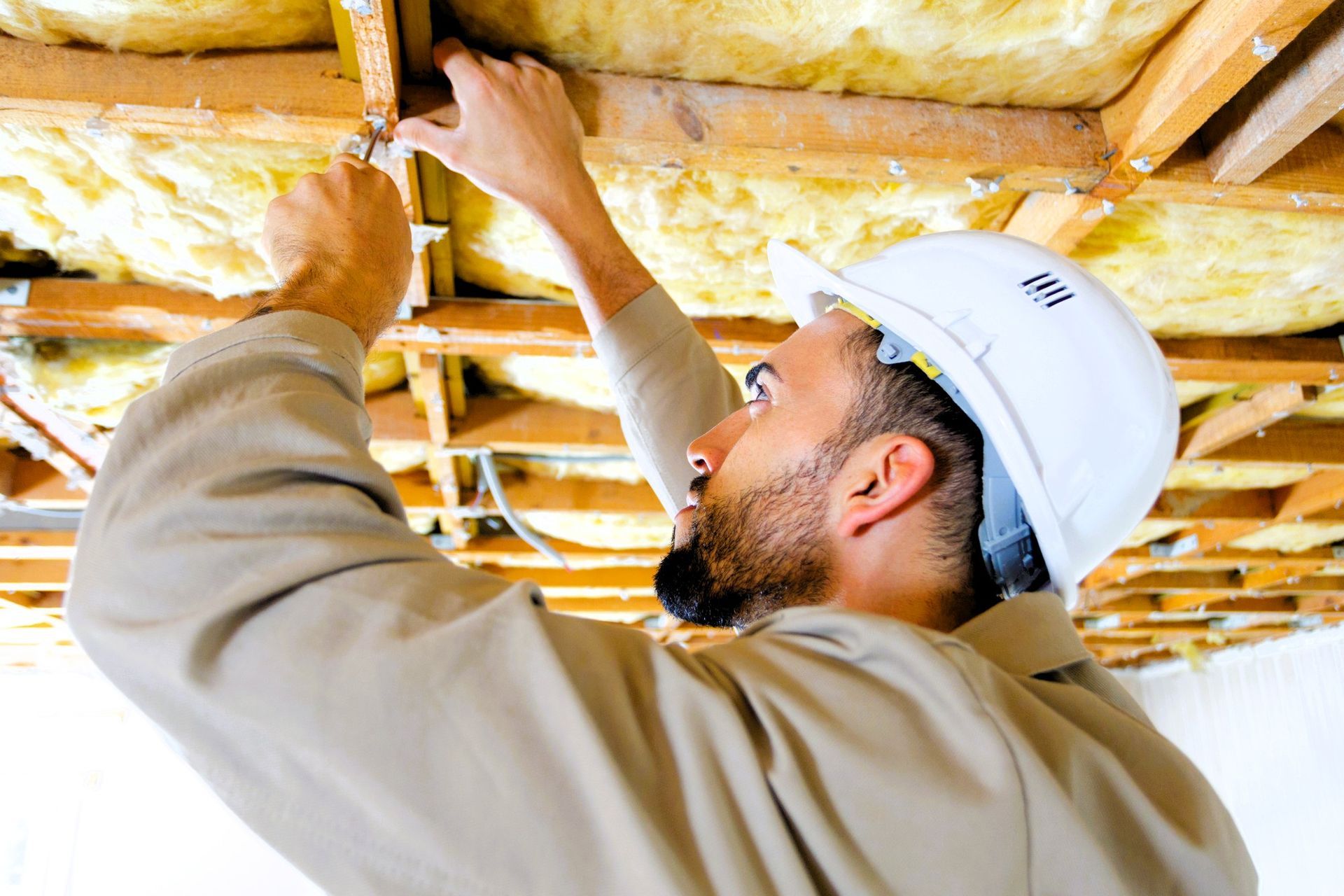 Basement finishing contractor wearing a hard hat installing insulation in the ceiling of a basement