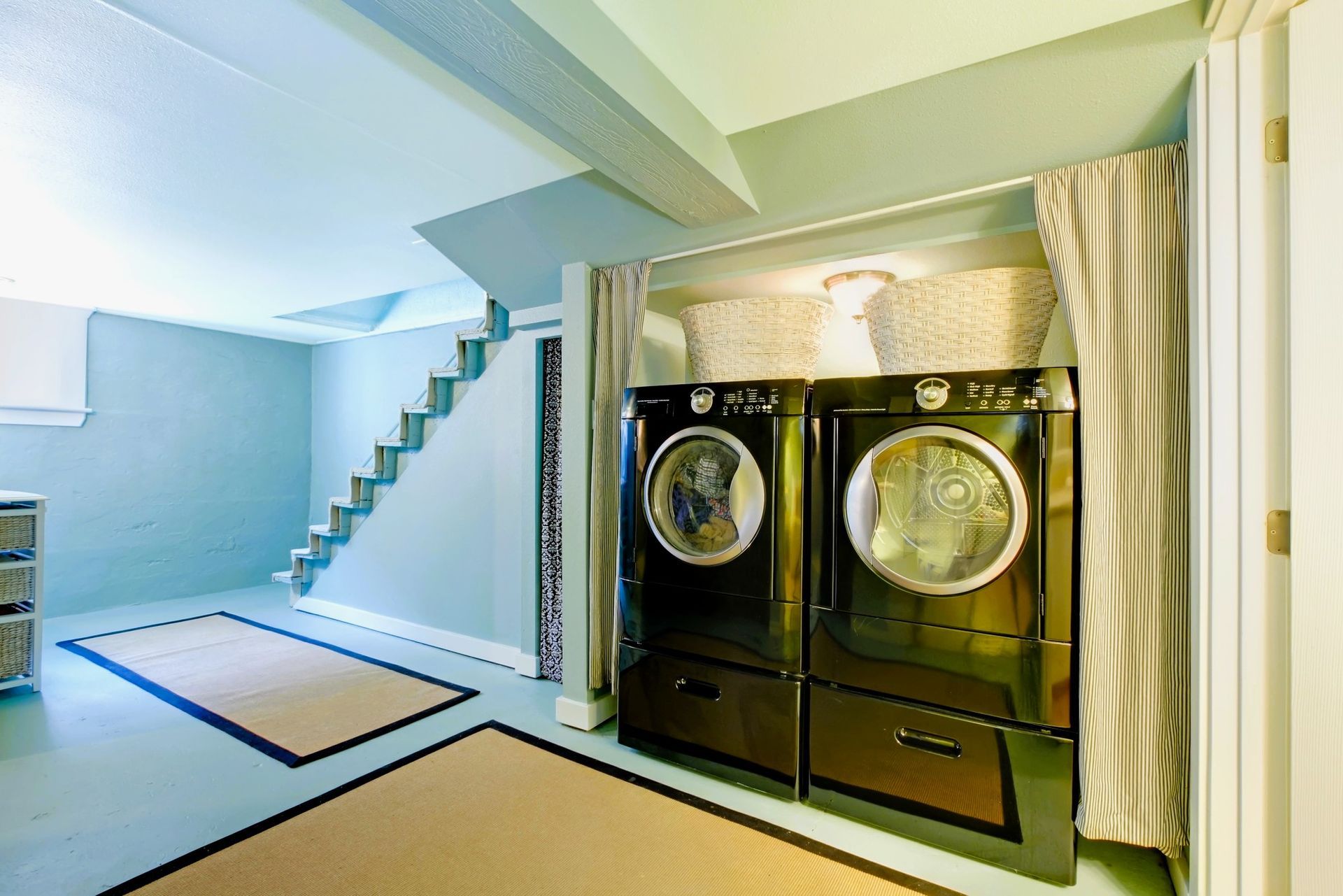 Modern laundry room with black washer and dryer, lit lamps above, adjacent to staircase.