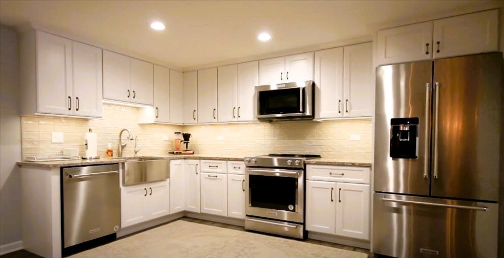 Basement kitchen with stainless steel appliances, white cabinets, and beige backsplash.