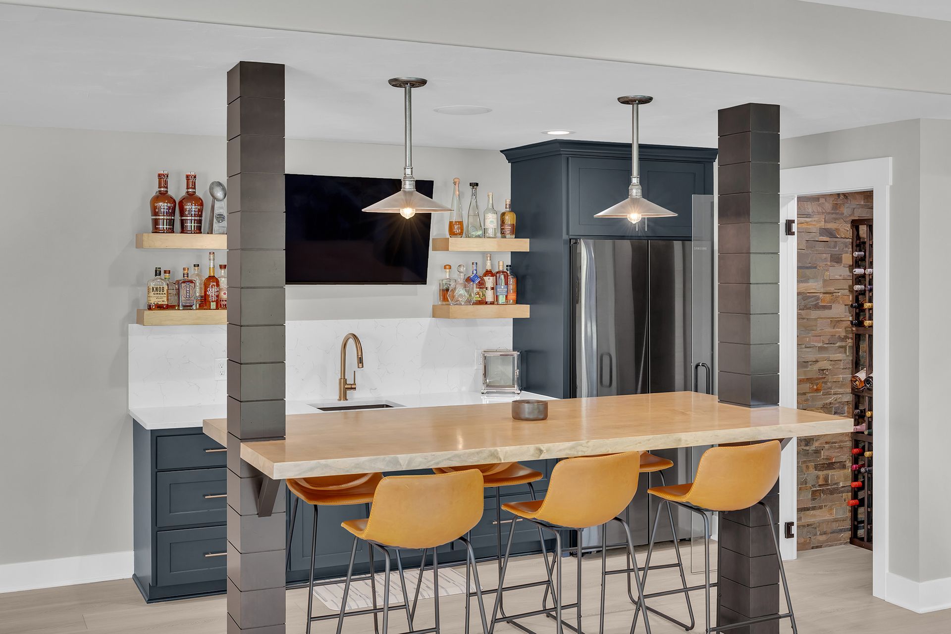 A basement kitchenette with a bar and stools and a refrigerator.
