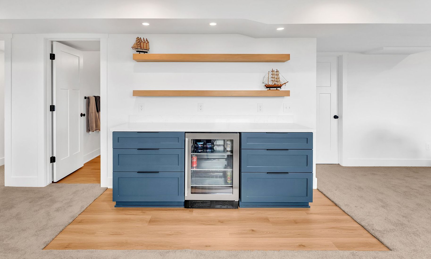 A basement dry bar with blue cabinets and a stainless steel refrigerator.
